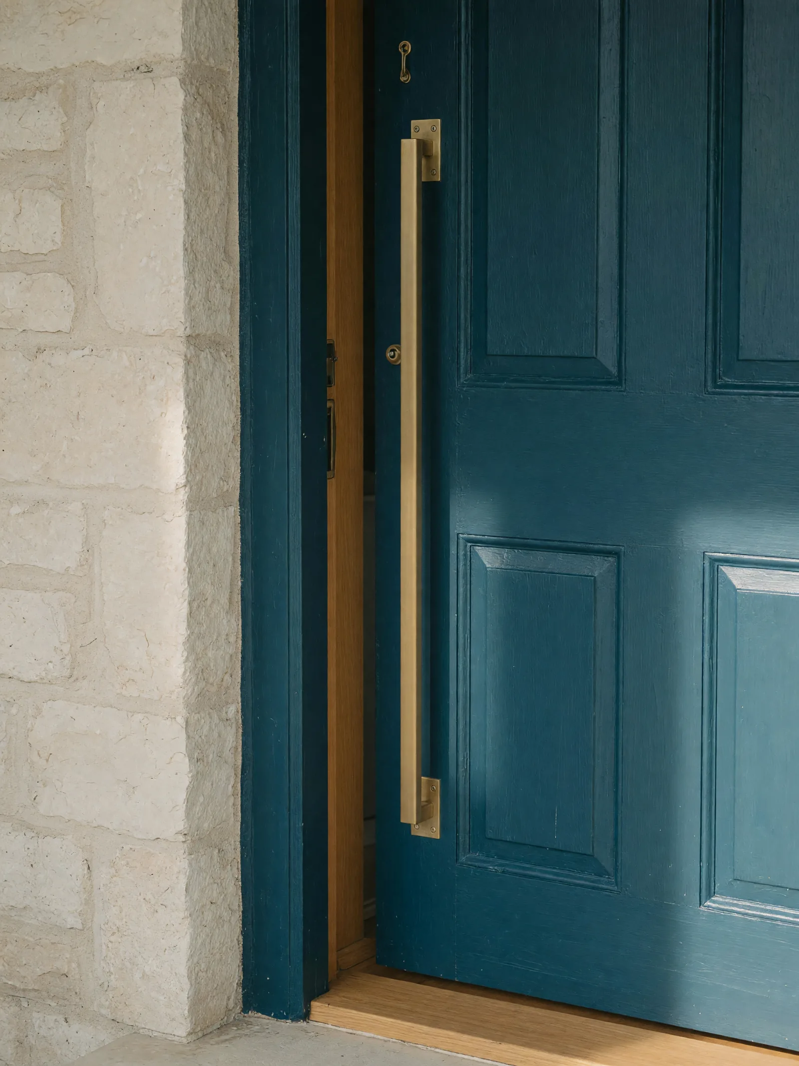 A deep blue door with a long brass handle beside a pale stone wall